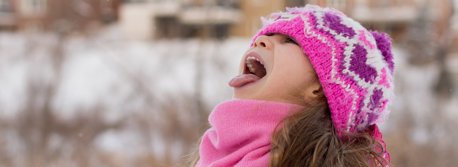 a girl wearing a pink hat catching snowflakes