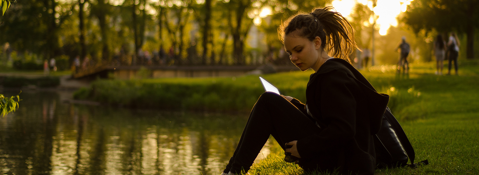 young woman reading and sitting on a river bank