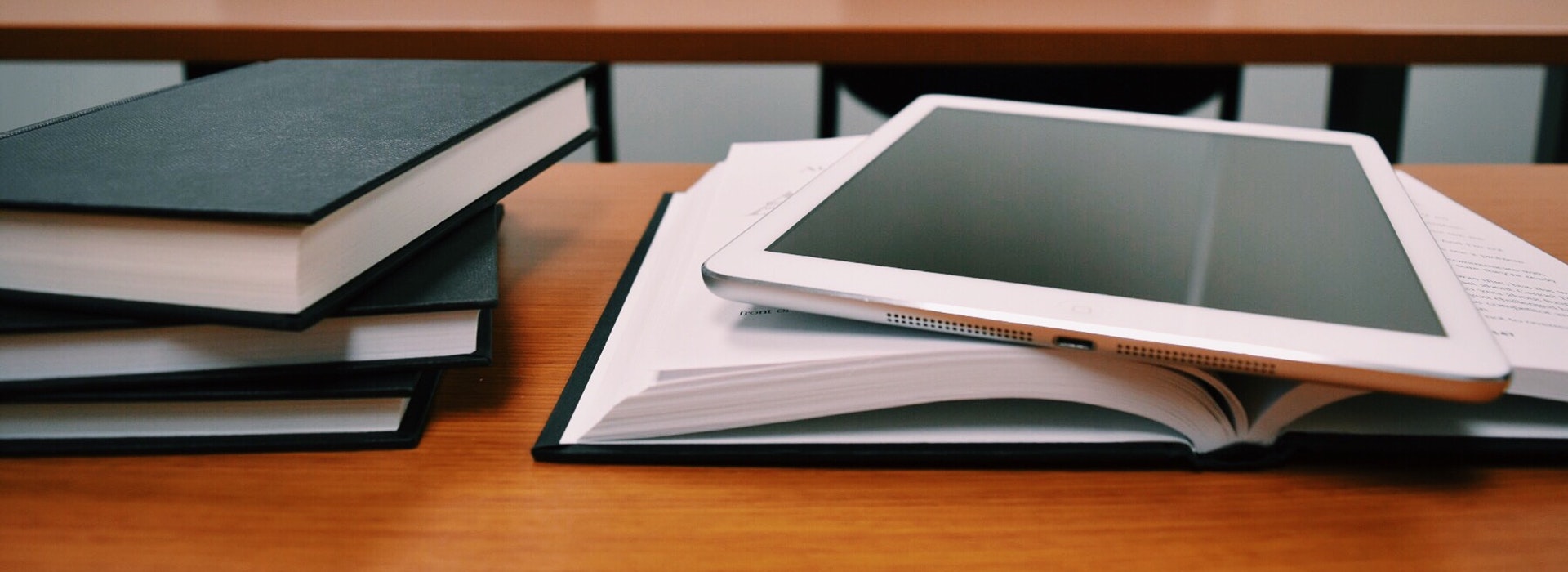 Livres noirs et un iPad blanc empilés sur un bureau en bois.