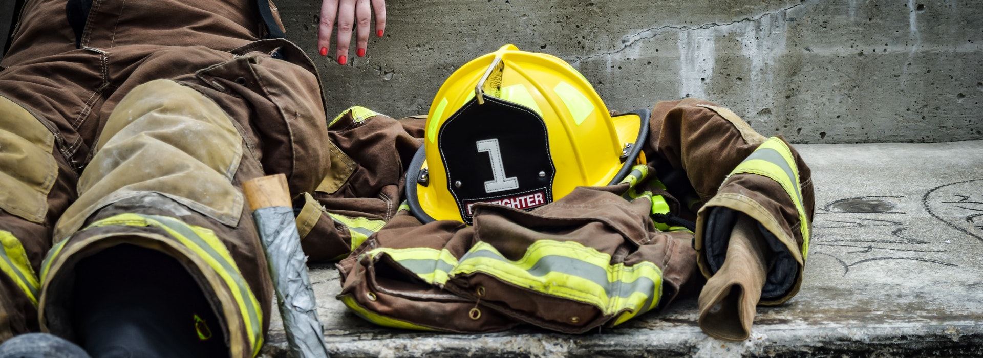 A yellow hardhat and firefighter’s jacket sits next to a firefighter sitting on the ground