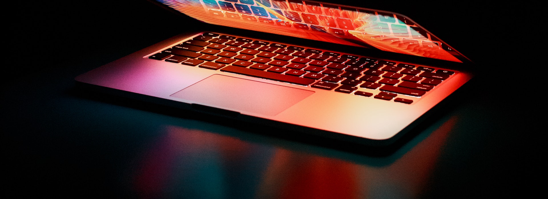 A multicolored laptop glows against a black backdrop