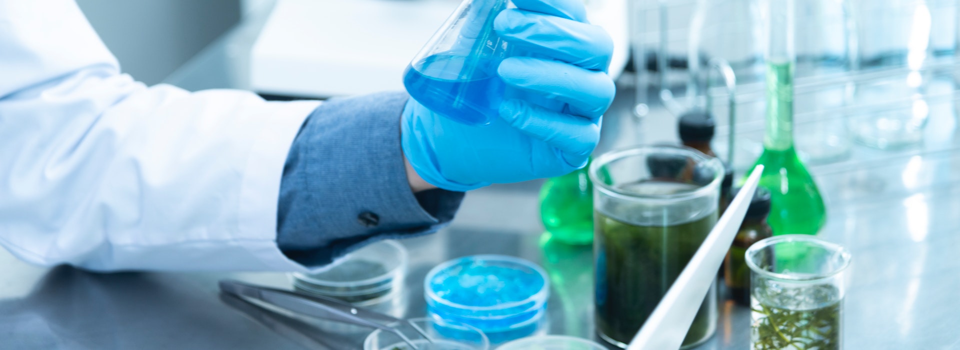 Photo d'une main gantée de bleu tenant un tube à essai chimique