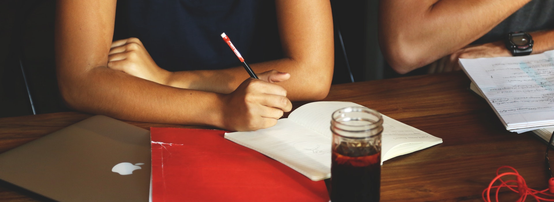 Closeup photo of a woman writing in a red notebook on a desk with a cup of coffee in front of her